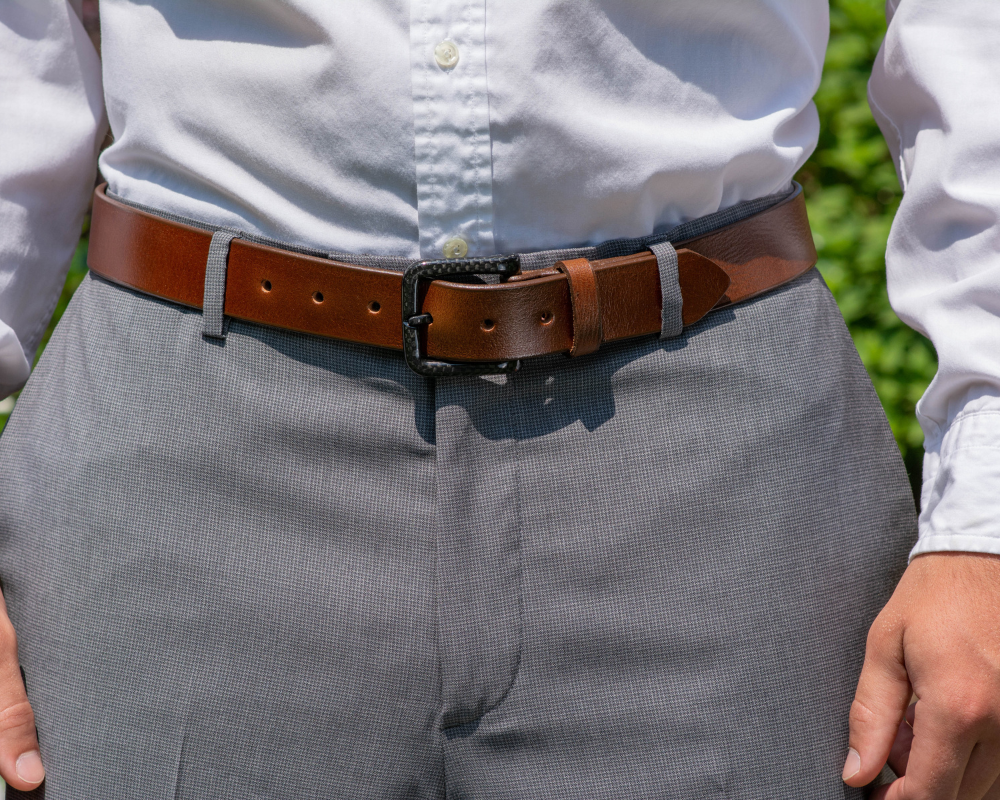 Image of a man wearing grey slacks, a white button-up shirt and The Specialist Brown Leather Dress Belt. The Specialist Brown has a light brown leather strap with a curved black carbon fiber buckle.